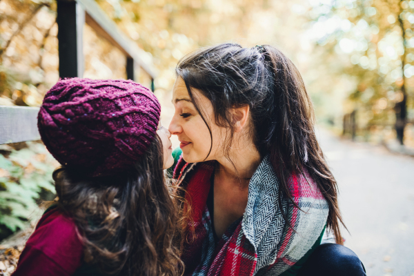 A portrait of young mother with a toddler daughter touching noses in forest in autumn nature.