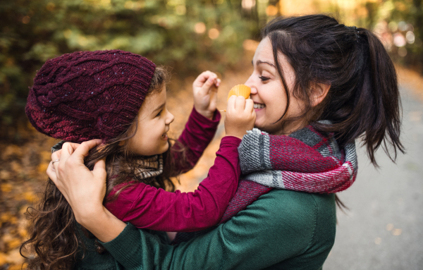 A portrait of young mother with a toddler daughter in forest in autumn nature.