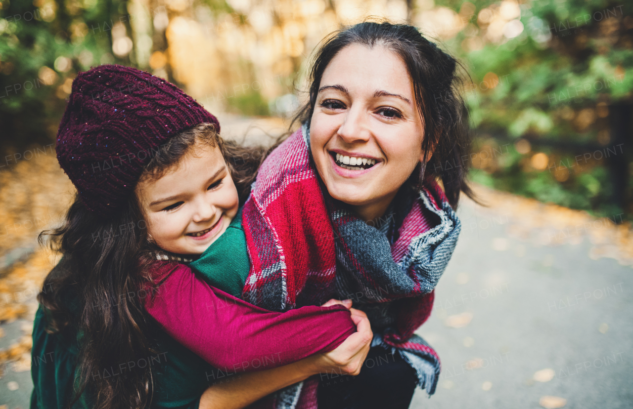 A young mother giving a toddler daughter a piggyback ride in forest in autumn nature.