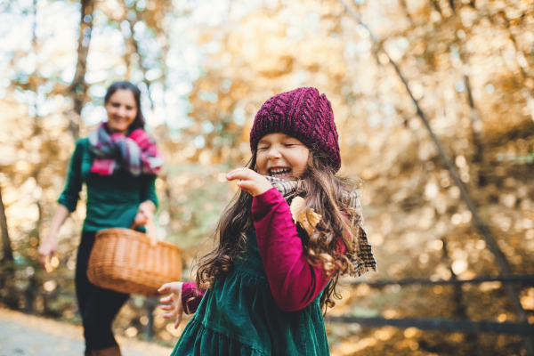 A portrait of toddler girl with mother in forest in autumn nature, having fun.