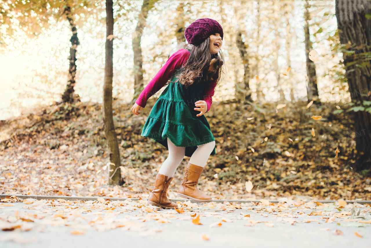 A portrait of a happy small toddler girl running in forest in autumn nature.