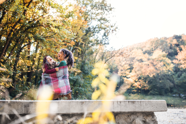 A portrait of young mother with a toddler daughter having fun in forest in autumn nature. Copy space.