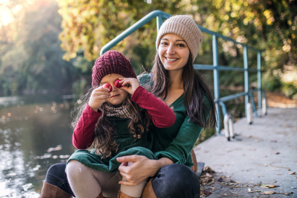 A portrait of young mother with a toddler daughter sitting in forest in autumn nature, having fun.