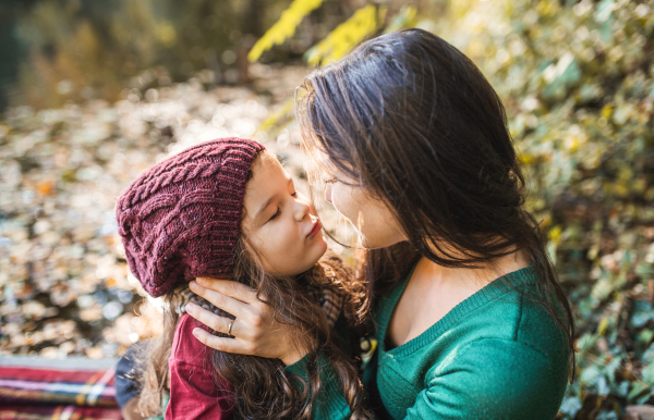 A portrait of young mother with a toddler daughter hugging and kissing in forest in autumn nature.