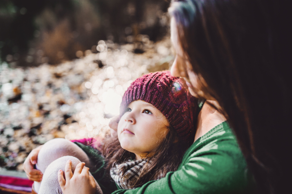 An unrecognizable young mother with a toddler daughter sitting in forest in autumn nature.