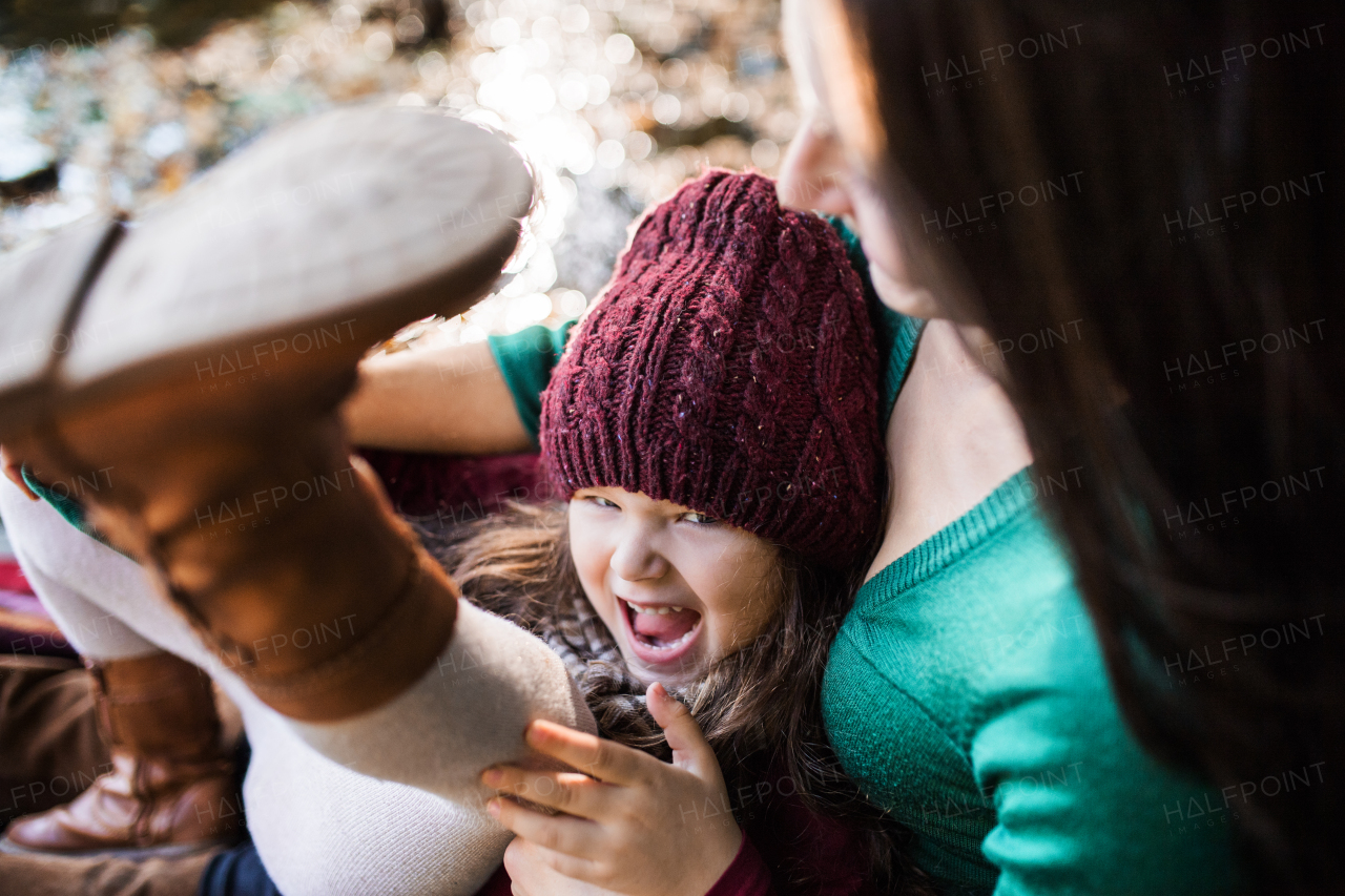 An unrecognizable young mother with a toddler daughter sitting in forest in autumn nature.