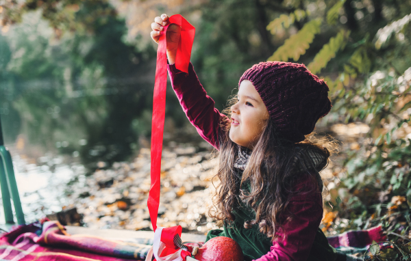 A portrait of a small toddler girl sitting in forest in autumn nature playing with ribbons.