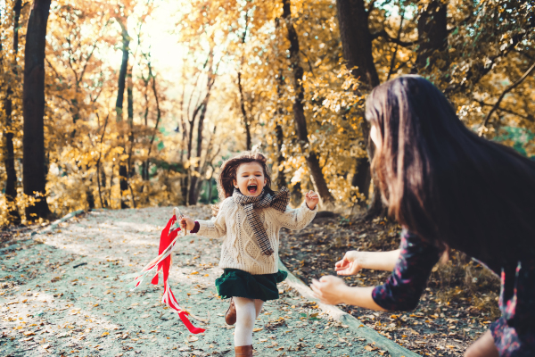 A portrait of young mother with a toddler daughter running in forest in autumn nature.