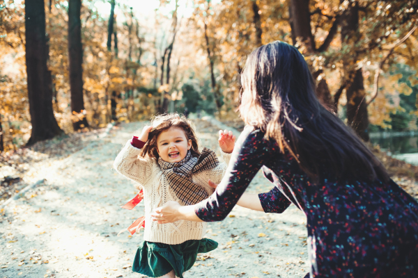 A portrait of young mother with a toddler daughter running in forest in autumn nature.