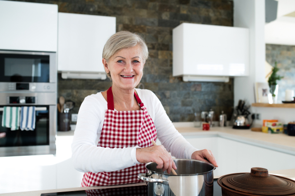 Beautiful senior woman in the kitchen cooking, mixing food in a pot.