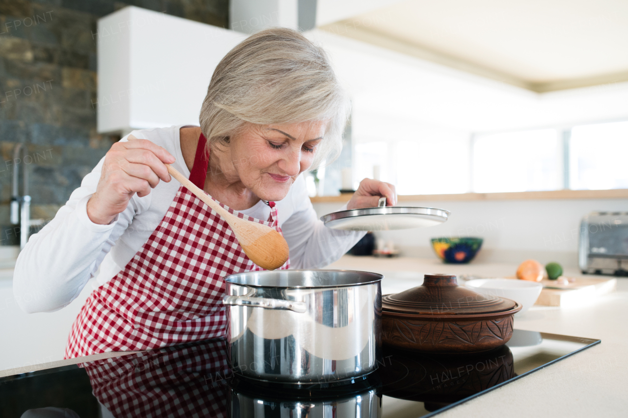 Beautiful senior woman in the kitchen cooking, mixing food in a pot, smelling it.