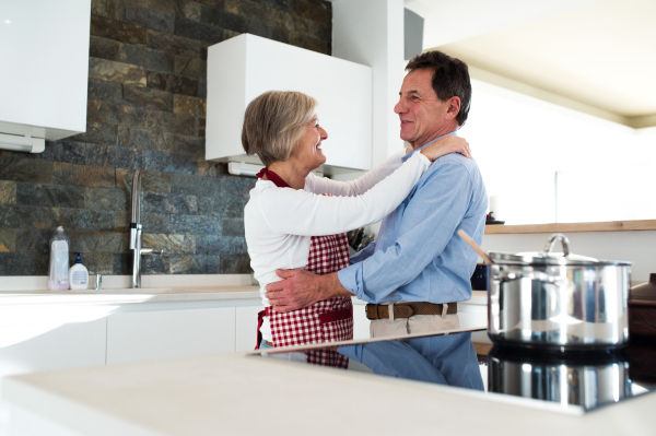 Senior woman and man in the kitchen cooking and dancing together.