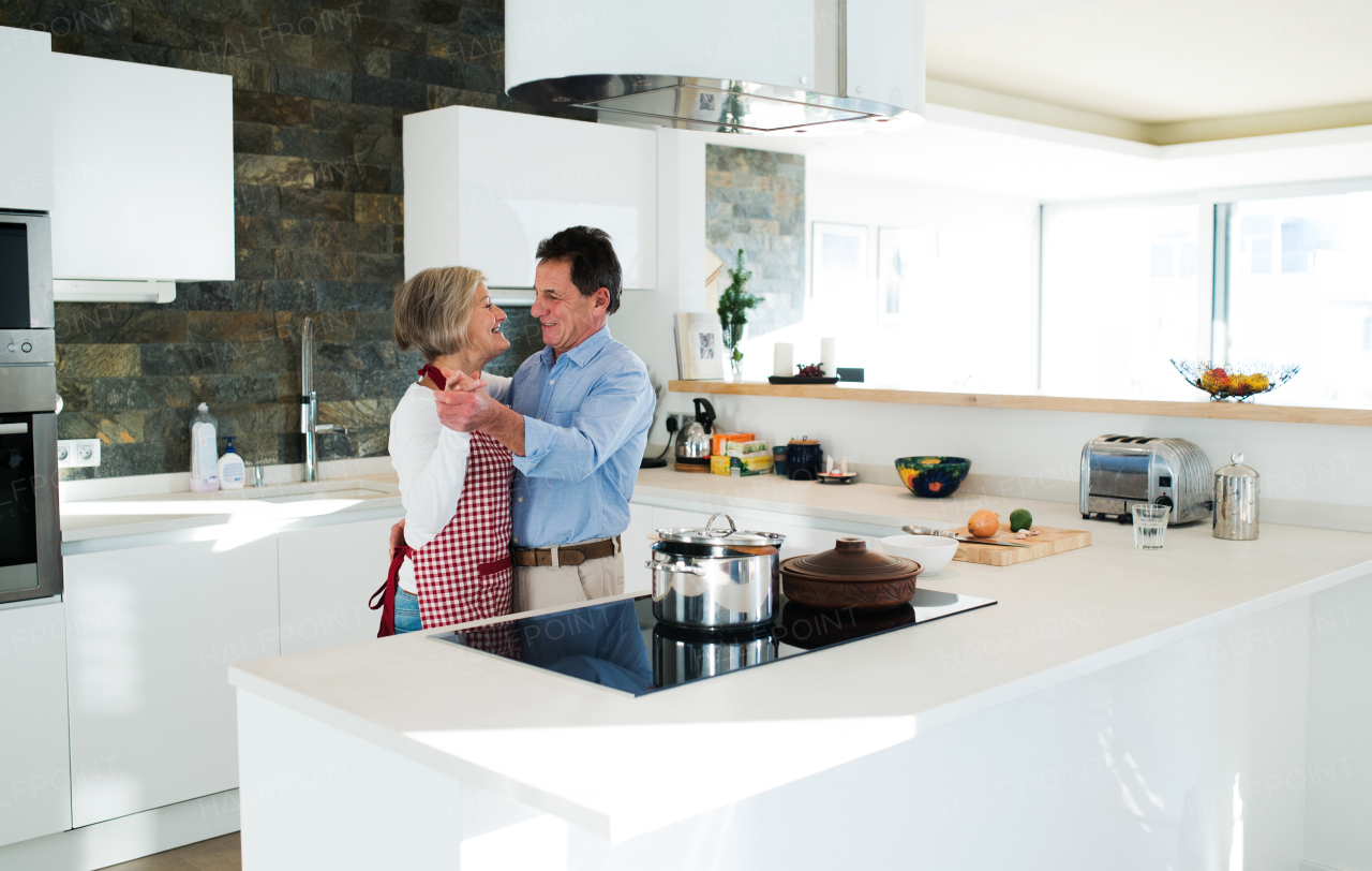 Senior woman and man in the kitchen cooking and dancing together.