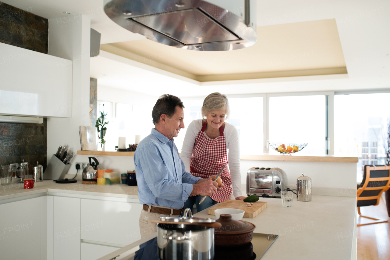 Senior couple in the kitchen cooking together, man cutting onion talking to his wife