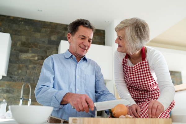 Senior couple in the kitchen cooking together, man cutting onion talking to his wife