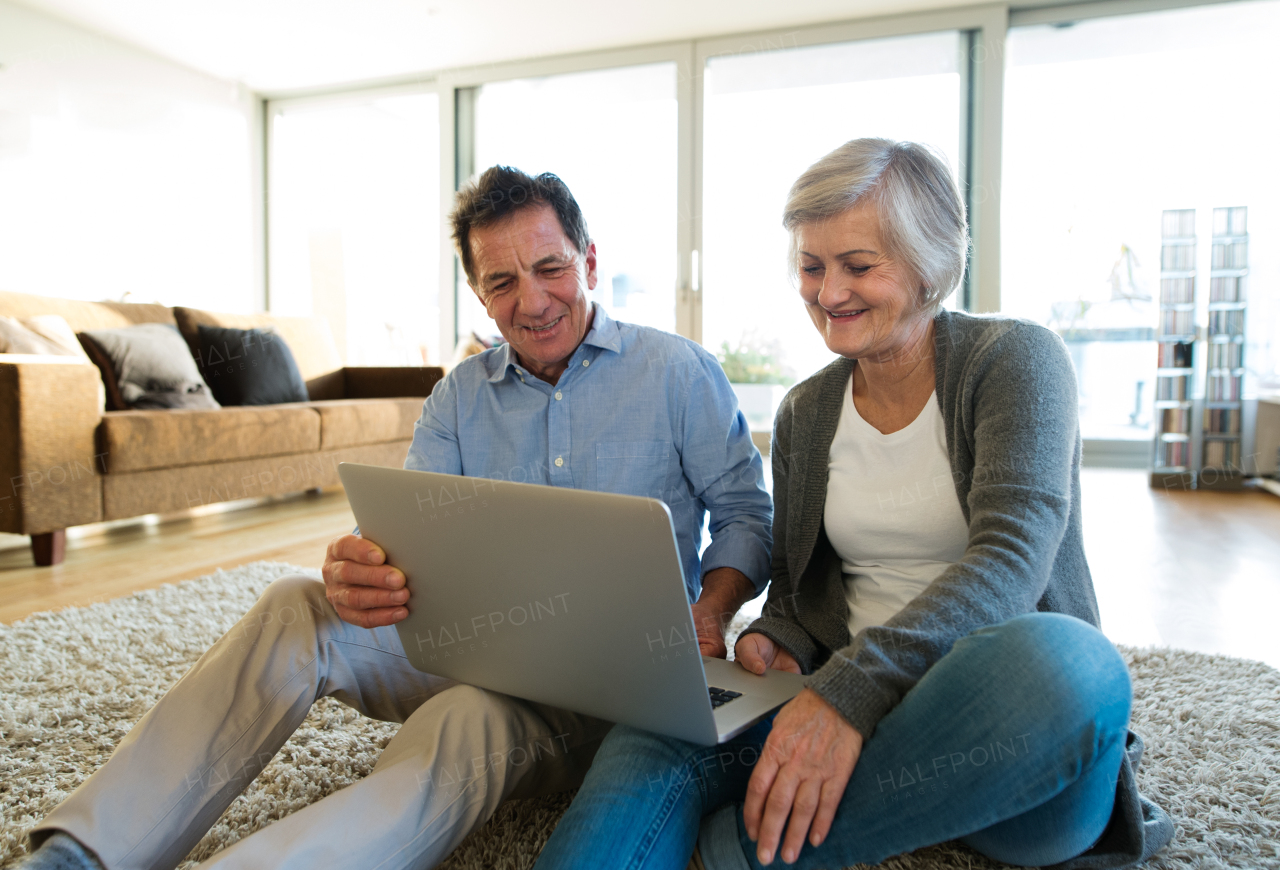 Beautiful senior woman and man sitting on the floor in living room, working on laptop