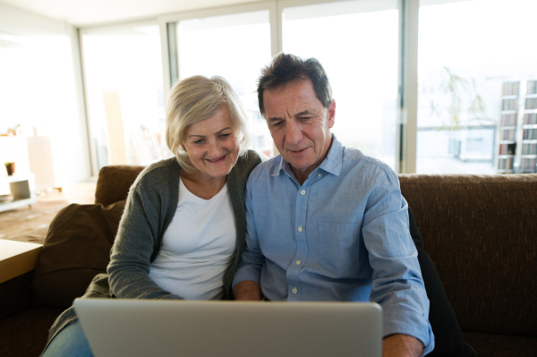 Beautiful senior woman and man sitting on a couch in living room, working on laptop