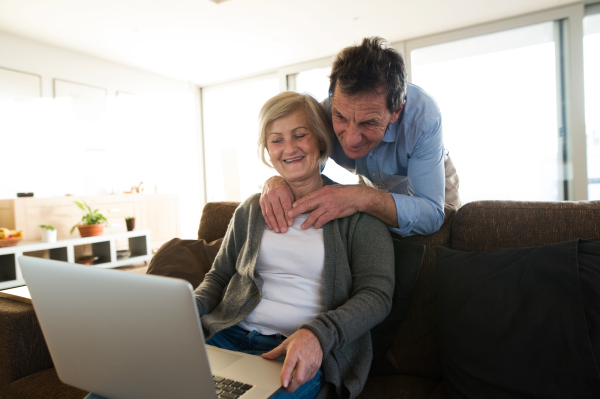 Beautiful senior couple on a couch in living room, woman working on laptop, man hugging her.