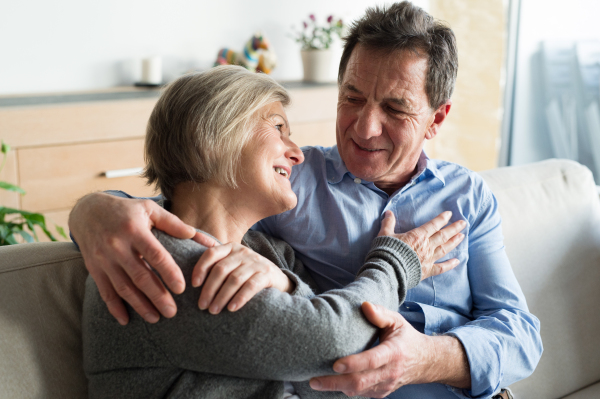 Beautiful senior woman and man sitting on a couch in living room, hugging