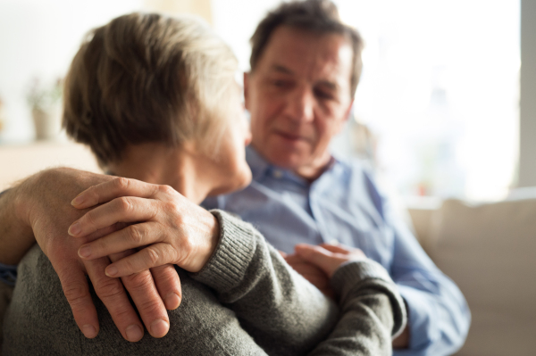 Beautiful senior woman and man sitting on a couch in living room, hugging