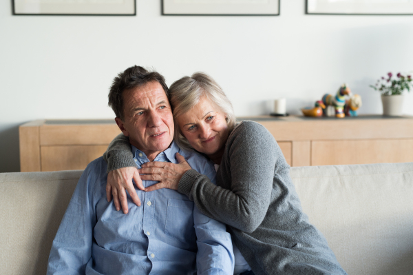 Beautiful senior woman and man sitting on a couch in living room, hugging