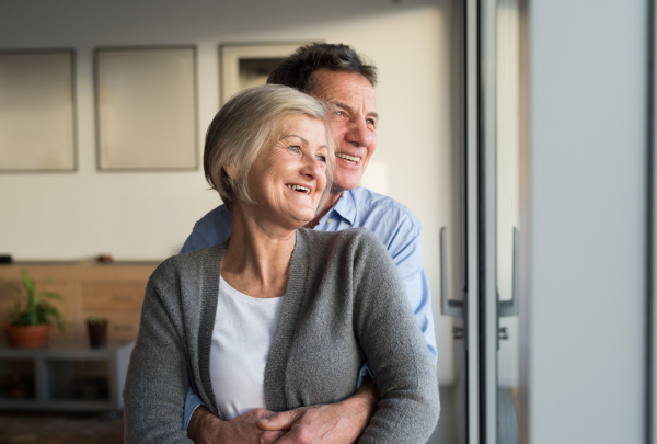 Beautiful senior woman and man in their living room standing at the window, hugging