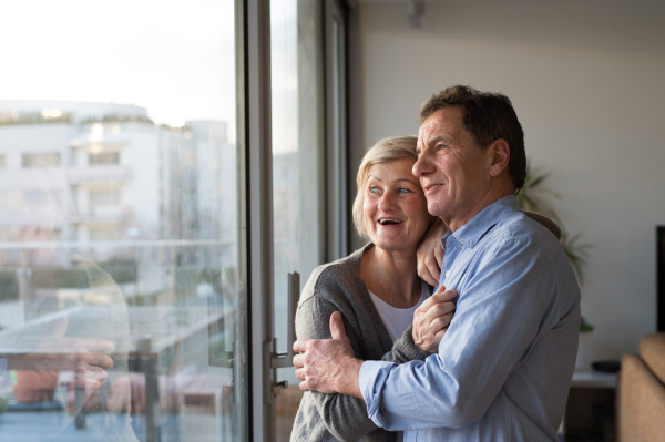 Beautiful senior woman and man in their living room standing at the window, hugging