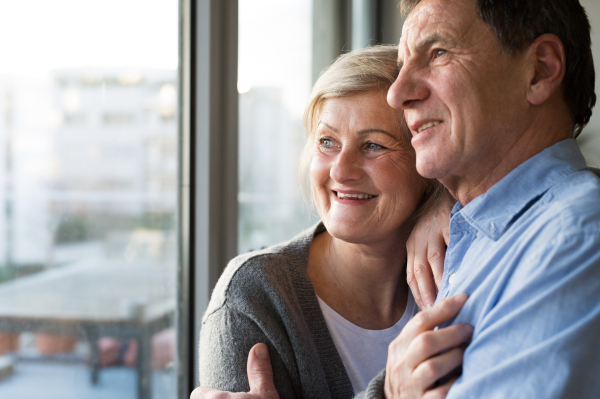 Beautiful senior woman and man in their living room standing at the window, hugging