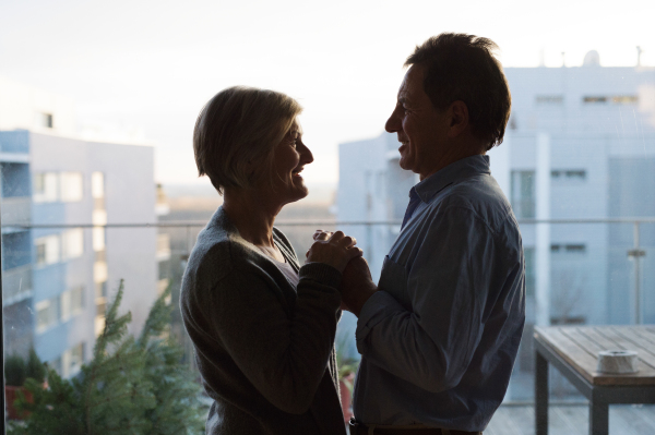 Silhouette of senior couple in love standing on a balcony against each other, holding hands, smiling