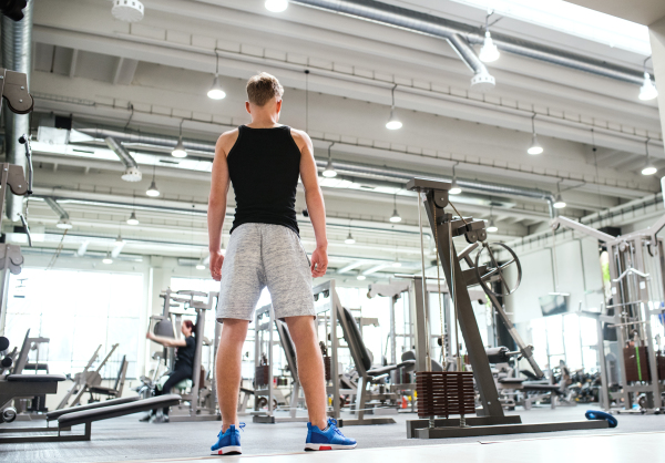 Young man in modern crossfit gym, standing. Rear view. Copy space.