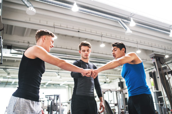 Young man friends standing and talking in modern crossfit gym, making fist bump.