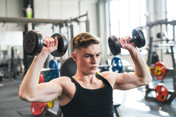 Young fit men doing strength training, exercising with dumbbells in modern gym.