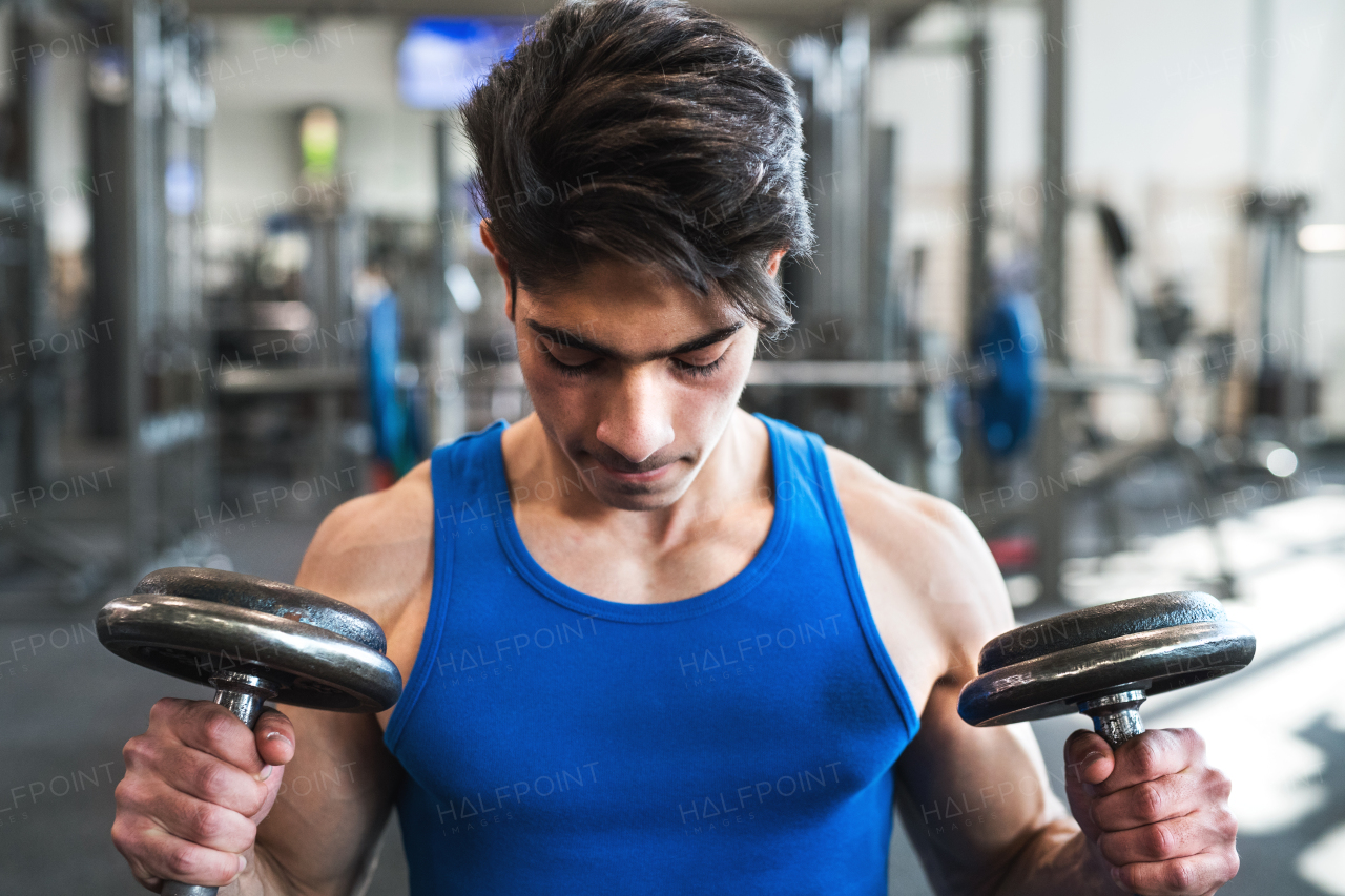 Fit hispanic man doing strength training, exercising with dumbbells in modern gym.