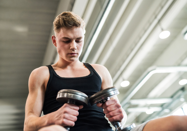 Young fit men doing strength training, exercising with dumbbells in modern gym.