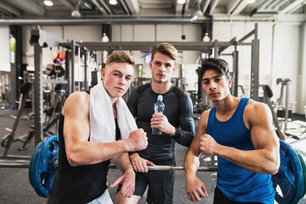 Young male friends in modern crossfit gym, standing and showing muscles.