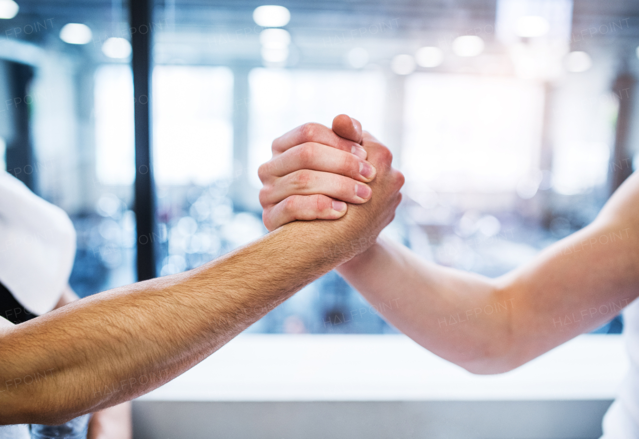 A friendly handshake of two young unrecognizable men in crossfit gym. A close-up.