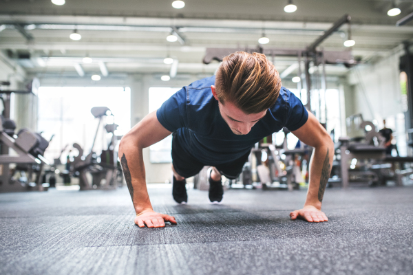 Fit man doing strength training, doing push ups in modern gym.