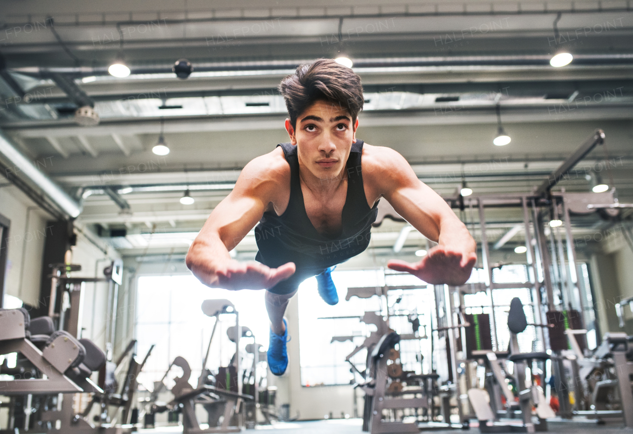 Hispanic young fit man doing strength training, doing jumping push ups in modern gym.