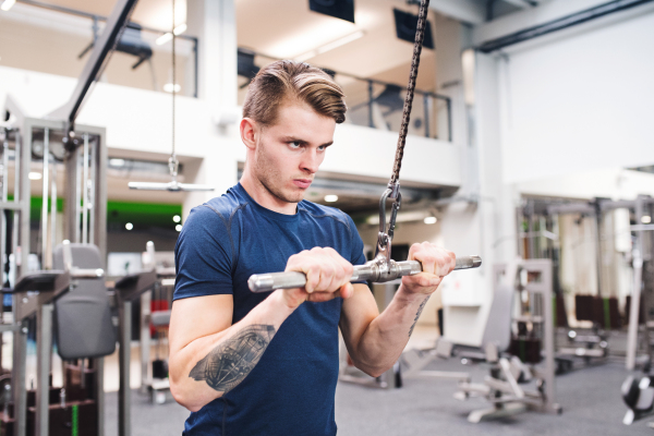 Young handsome fit man working out on pull-down machine in gym. Bodybuilder exercising with cable weight machine.