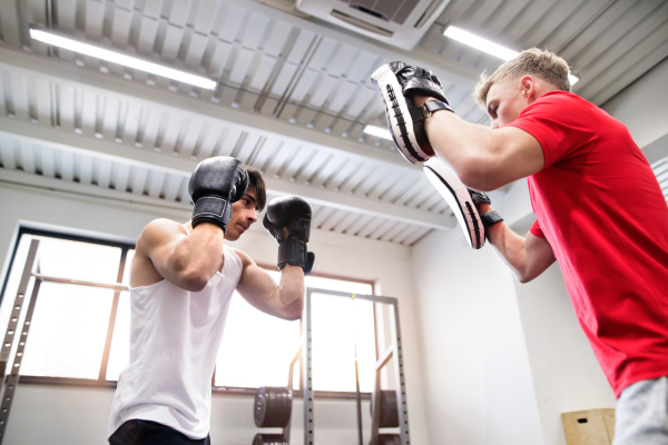 Handsome fit hispanic man in gym boxing with his personal trainer