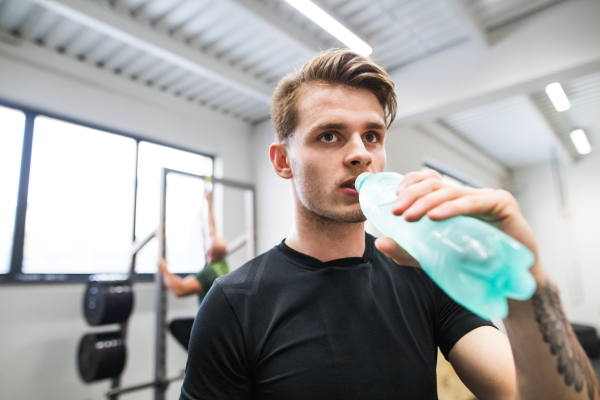 Young handsome fit man in gym, resting in between exercises, drinking water.