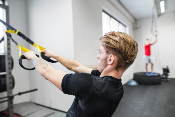 Young handsome fit man in gym working out with suspension straps.