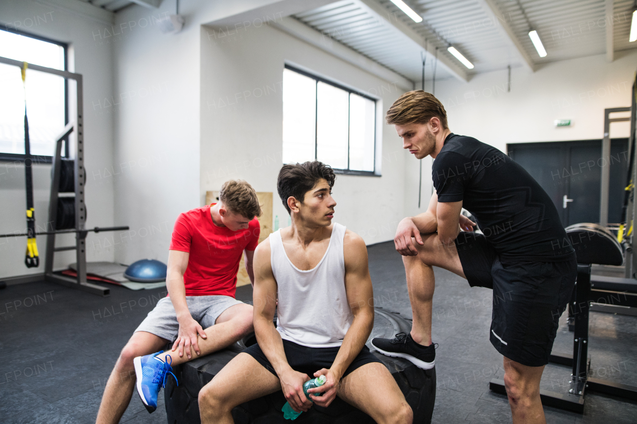 Three young fit men in crossfit gym resting after an exercise, talking.