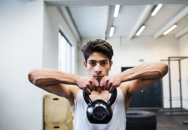 Fit hispanic man doing strength training, lifting kettlebell in crossfit gym.