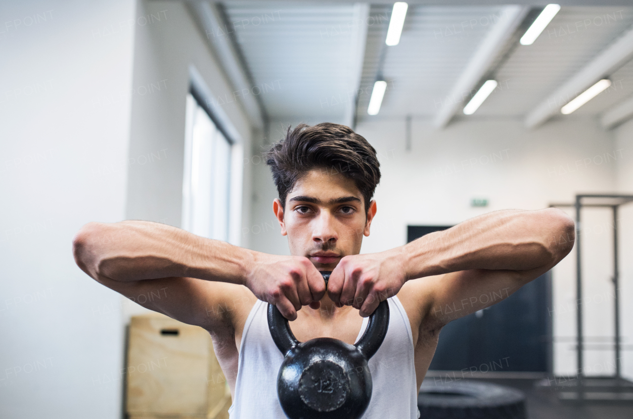 Fit hispanic man doing strength training, lifting kettlebell in crossfit gym.