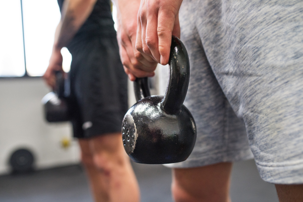 Unrecognizable young fit men in crossfit gym working out, doing kettlebell swings.