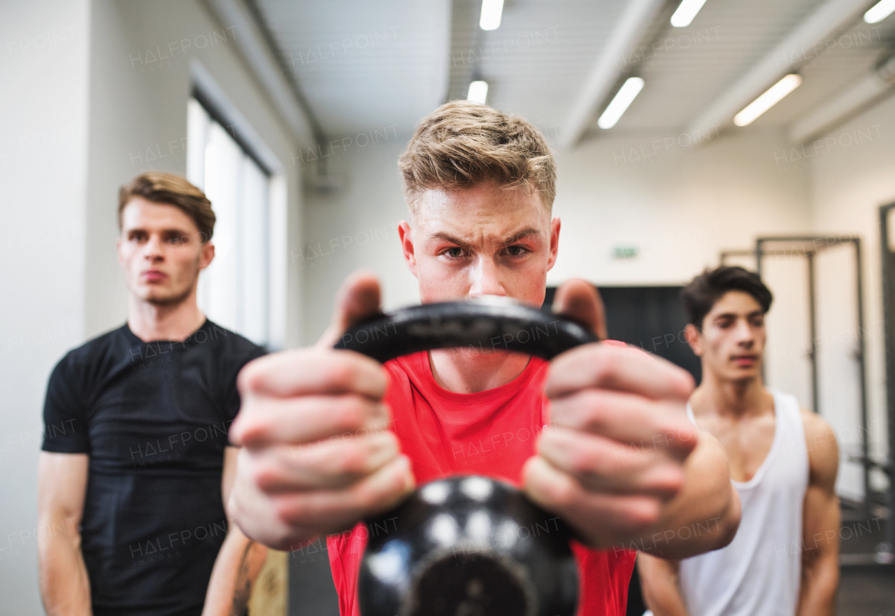 Three young fit men in crossfit gym working out, doing kettlebell swings.