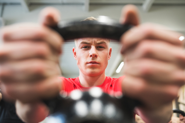 Fit hispanic man doing strength training, lifting kettlebell in crossfit gym. Close-up.