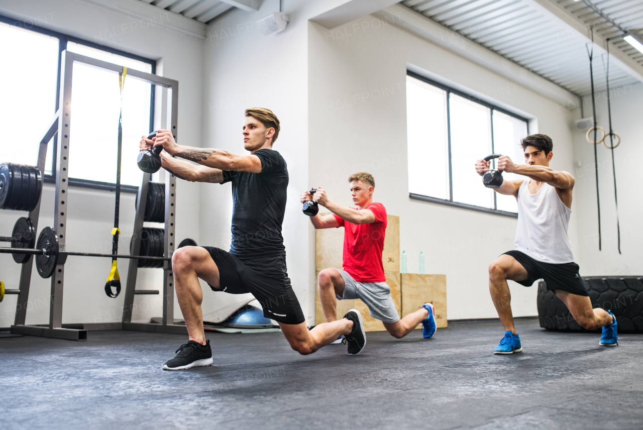 Three young fit men in crossfit gym working out with kettlebells.