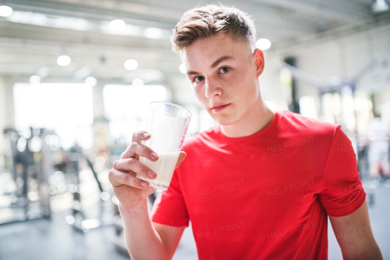 A young fit men in crossfit gym holding a glass with protein drink. Copy space.